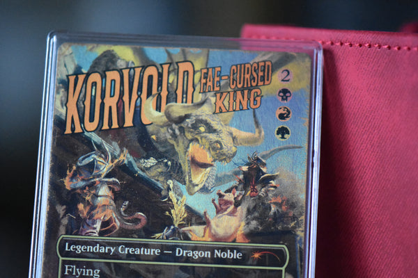 Korvold Rainbow Foil PCG 9.5 in a Slim Player Slab next to a red deckbox - closeup