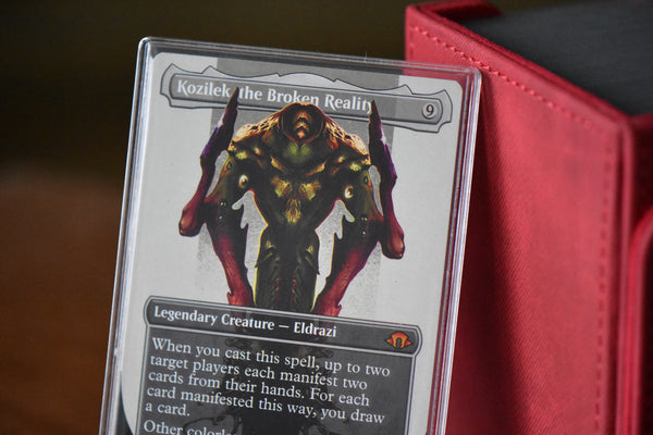 Kozilek Borderless PCG 9 Mint in a Slim Player Slab next to a red deckbox - closeup angle