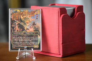 Korvold Rainbow Foil PCG 9.5 in a Slim Player Slab next to a red deckbox - front view