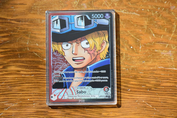 Sabo OP13 Alt Leader PCG 10 Gem Mint in a Slim Player Slab on a wooden shelf - front.